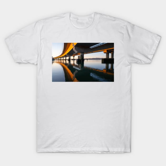 Morning sun strikes side Tauranga Harbour Bridge in golden hue reflected leading lines into calm water below T-Shirt by brians101